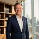 Portrait professionnel de Bruno Pesery en costume sombre dans un bureau exécutif moderne avec vue sur la ville